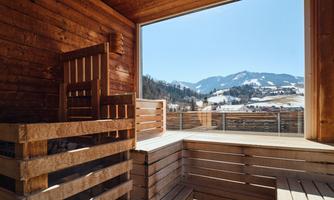 A cozy wooden sauna with a view of a snowy mountain landscape. The clear sky and mountains create a relaxing atmosphere.