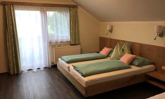 A cozy bedroom with two beds and colorful pillows. Large windows let in plenty of light and offer a view outside.