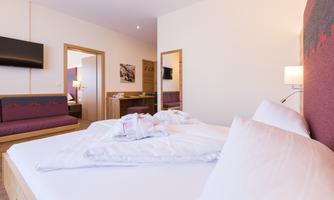 A modern hotel room with a large bed and a cozy seating area. The walls are bright, and the lighting creates a friendly atmosphere.