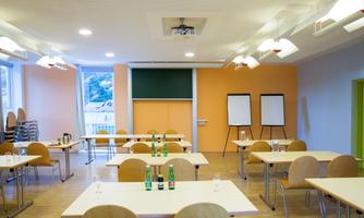 A modern seminar room with several tables and chairs. Water bottles are on the tables and some flip charts are ready.