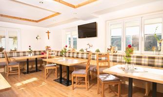 A cozy restaurant with wooden chairs and tables. The walls are bright, and the windows let in plenty of daylight.
