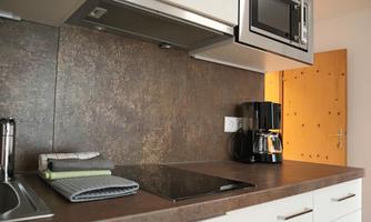A modern kitchen with a cooktop, a microwave, and a coffee machine. The walls are in neutral colors, and a door leads to another room.