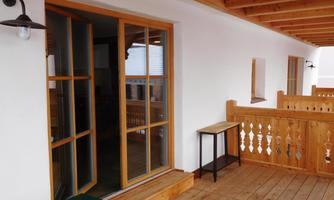 A balcony with a wooden railing and a table. The area is bright and inviting, with large windows leading to the interior.