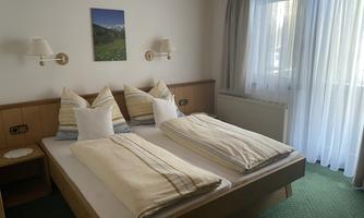 A bright bedroom with a double bed and two pillows. Large windows let in a lot of light and display a picturesque view.