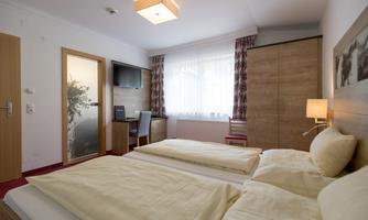 A cozy hotel room with two single beds, a desk, and a television. The room has plenty of daylight and a modern decor.