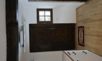 A cozy kitchen with a wooden floor and a dark wooden door. Next to the door is a small window and a welcome runner on the floor.