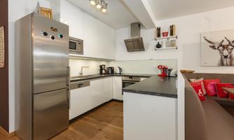 A modern kitchen with stainless steel appliances and white cabinets. The wooden floor and the cozy seating area create an inviting atmosphere.