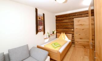A cozy bedroom with a single bed and a gray couch. The walls are made of wood, and there is a small decoration on the shelf.