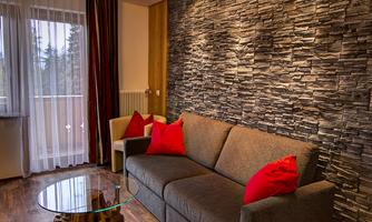 A cozy living room with a gray sofa and colorful cushions. The wall is designed with stone cladding, and there is a glass table.