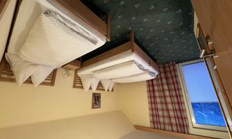 A cozy bedroom with two single beds and a window. The walls are painted in a warm yellow tone and the room has a simple, inviting style.