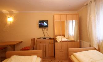 A simple room with two beds, a television, and a wardrobe. There is also a table and chairs in the bright room.