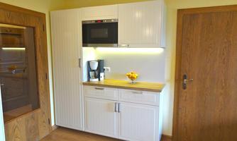 A modern kitchen with white cabinets and wooden surfaces. On the countertop, there is a coffee machine and a bowl of fruit.
