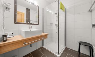 A modern bathroom with a glass shower and an elegant sink. The walls are painted in light colors, and there is a seating area.