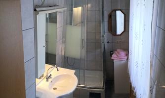 A bright bathroom with a shower and a sink. White tiles and a large window provide plenty of light.