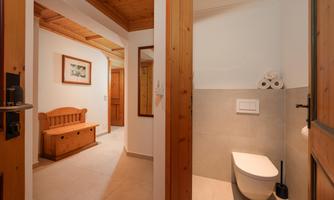 An inviting bathroom with a modern toilet and a wooden chair in the hallway. The walls are bright, and the atmosphere feels friendly and clean.