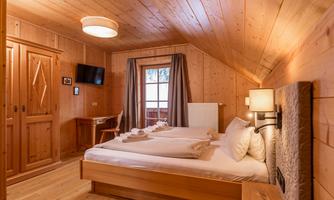 A cozy room with wooden paneling and a large window. There is a double bed, a table, and a television.