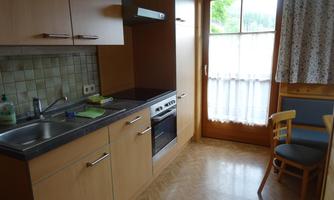 A simple kitchen with wooden cabinets and a sink. A lot of light comes in through the window.