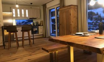 A modern kitchen with wooden furniture and large windows. The room has a cozy dining area and a warm atmosphere.