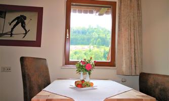 A cozy dining table with flowers and fruit. In the background, there is a window with a view of a green landscape.