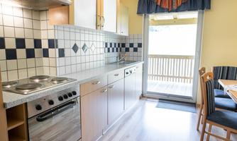 A modern kitchen with bright wood cabinets and a dining area. The view goes through a glass door to a balcony with a beautiful view.