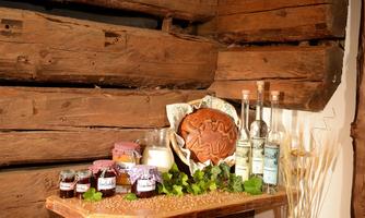 A wooden shelf with various treats stands against a rustic wall. This includes jam, schnapps, bread, and dairy products.
