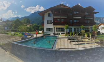 A modern building with several floors is located by a pool. In the background, green mountains and blue sky can be seen.
