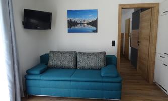 A modern living room with a blue sofa and a television on the wall. A picture of a city view hangs above the sofa.