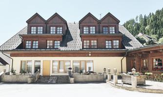 A comfortable building with wooden cladding and large windows. In the background, green mountains are visible.
