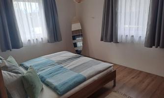 A bright bedroom with a double bed and large windows. Decorated with simple curtains and a large mirror.