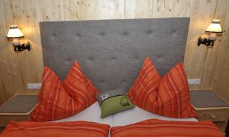 A cozy bedroom with a double bed and striking red pillows. The walls are made of wood, and there are two wall lamps on the side.