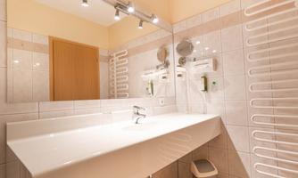 A modern bathroom with a large sink and a mirror. The walls are tiled in light colors and there are towel holders.