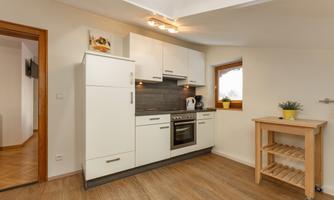 A modern kitchen with white furniture and a wooden countertop. The room has a window that lets natural light in.