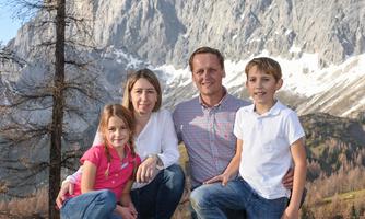 A family poses in nature in front of impressive mountains. The children as well as the adults are laughing and enjoying the view.