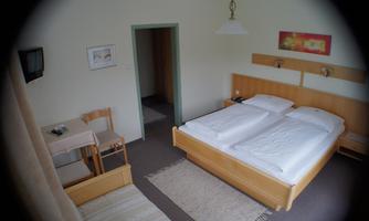 A simple hotel room with two single beds and a small table. The walls are light, and there is a television as well as carpeting.