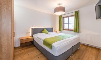 A cozy bedroom with a double bed and a window. The walls are light, and the room has a modern, calm atmosphere.
