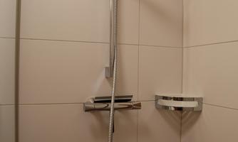 A modern shower with a handheld showerhead and a simple design. The walls are tiled and kept in light colors.