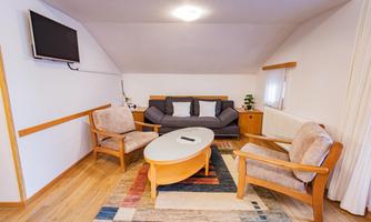 A cozy living room with a sofa and two chairs. A round table is in the middle, next to it a television on the wall.