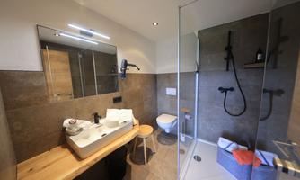 A modern bathroom with a large shower, a stylish sink, and wooden shelves. The walls are in neutral tones, creating a calm atmosphere.