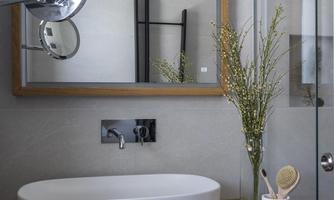 A modern bathroom with an elegant sink and a large mirror. The wooden shelf and the decorative vase add a stylish touch to the room.