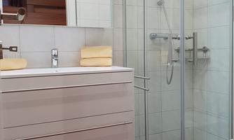 A modern bathroom with a glass shower and an elegant sink. The walls are tiled in light colors and the floor is red.