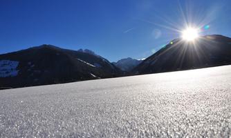 A majestic snowy landscape with a radiant blue sky and the sun rising over the mountains. The frozen surface sparkles in the light.