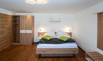 A modern bedroom with a large bed and two pillows. The room has wood details and a cozy atmosphere.