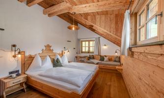 A cozy bedroom with a wooden ceiling and modern lighting elements. There is a double bed and a seating area with a window that lets in plenty of daylight.