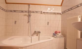 A modern bathroom with an oval bathtub and bright tiled floor. Some towels in different colors are placed on the edge.