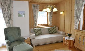 A cozy living space with wooden paneling and bright light. The furniture is simple and inviting, with a small table and a flower arrangement.