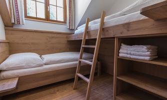 A cozy bedroom with a lower and upper bed made of wood. The room contains a ladder and folded towels on a shelf.