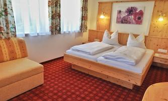 A cozy hotel room with two beds and a comfortable sofa. Large windows let in plenty of daylight and create an inviting atmosphere.