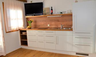 Modern kitchen with white cabinets and a wooden countertop. A television and some decorative items are visible.