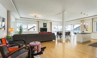 A modern apartment with an open living area and large windows. The furnishings are stylish and colorful, with comfortable furniture and a dining table.