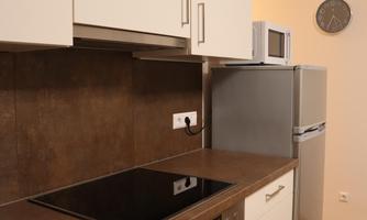 A modern kitchen with a cooktop, an oven, and a refrigerator. The furniture is in light colors and offers plenty of storage space.